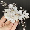 Une main tenant une pince à cheveux fleur en perle de cristal pour mariage, avec des fleurs blanches et des accents dorés dél