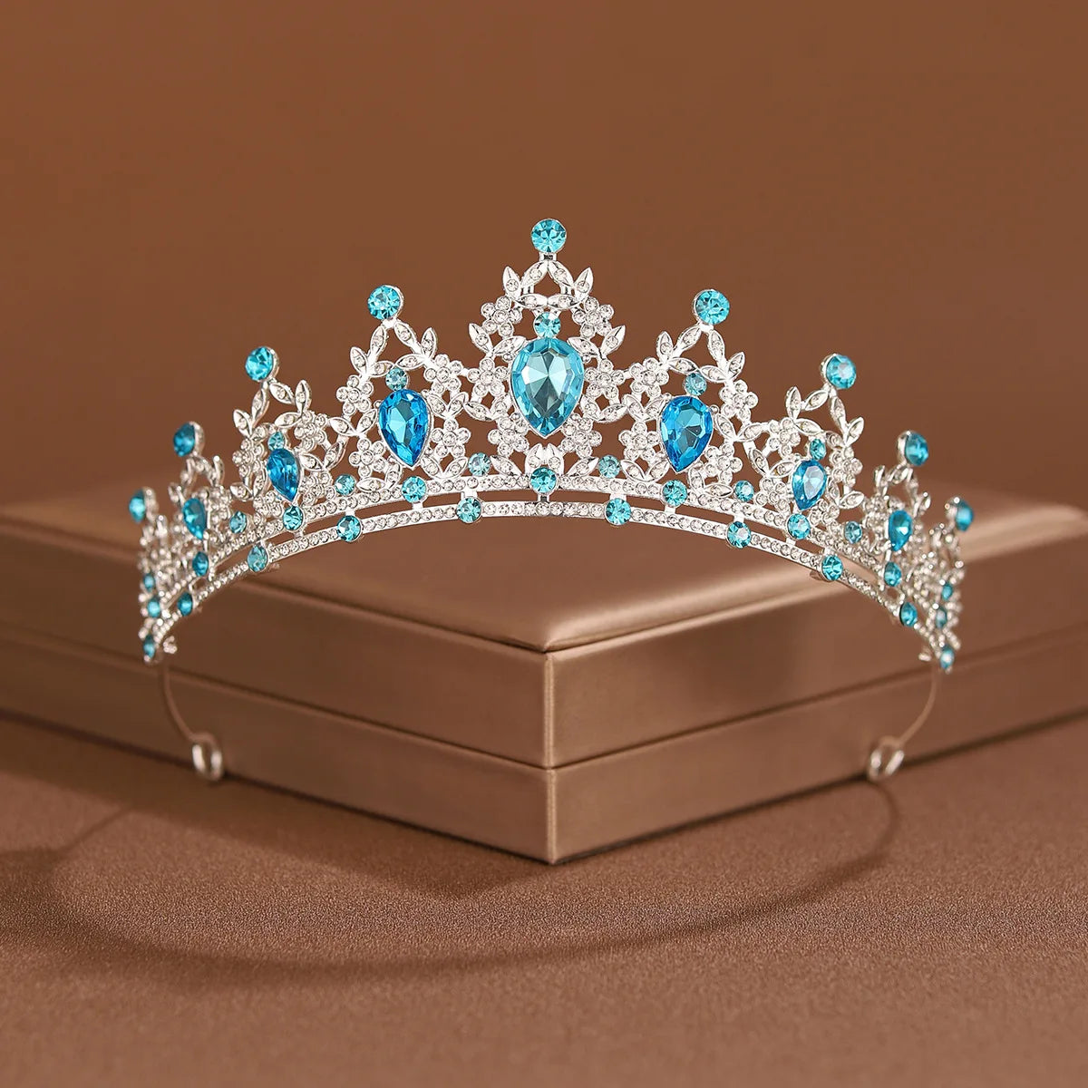 An elegant crystal baroque bridal tiara headpiece with blue gemstones displayed on a box.