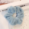 Une paire de pinces à cheveux en tricot flou bleu clair posées sur une surface blanche.