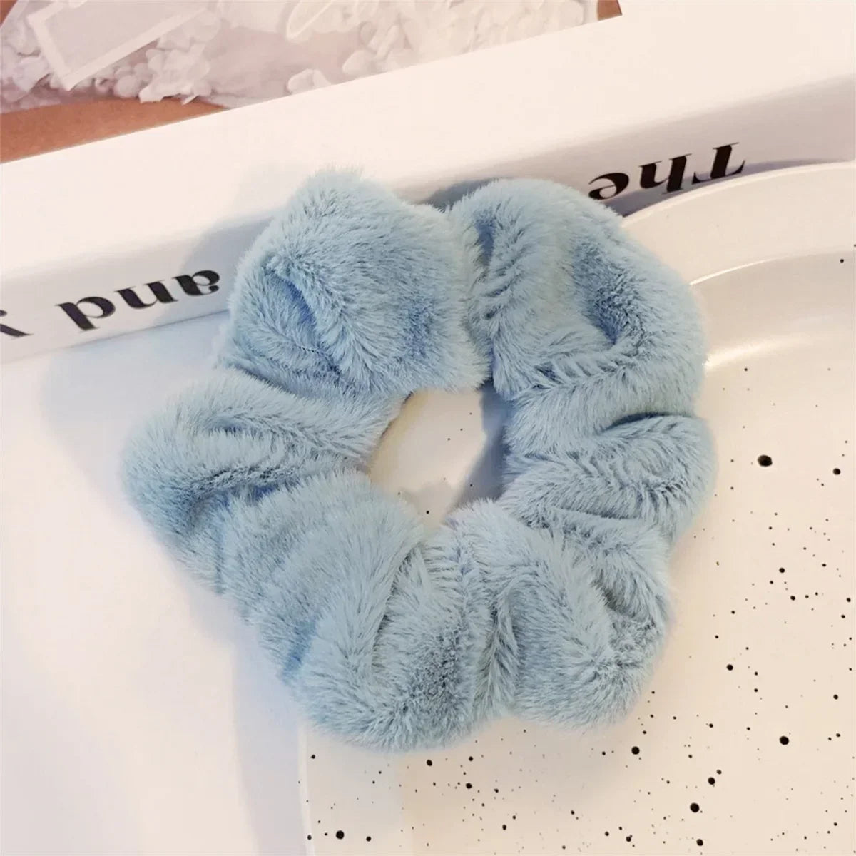 Une paire de pinces à cheveux en tricot flou bleu clair posées sur une surface blanche.