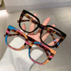 Eine Hand hält eine trendige, große, quadratische Brille mit Leopardenmuster.