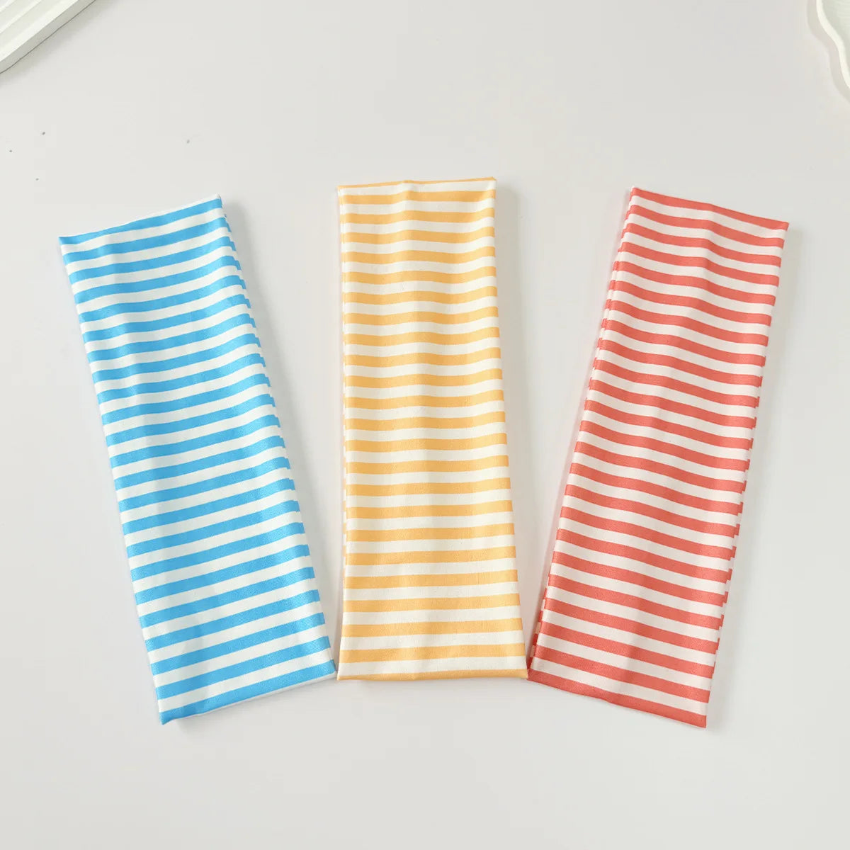 Trois élastiques pour cheveux à rayures bleues, oranges et rouges sont présentés sur une surface blanche.