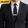 A close-up of a man wearing a dark suit jacket and white shirt with a navy blue tie featuring a silver tie clip.