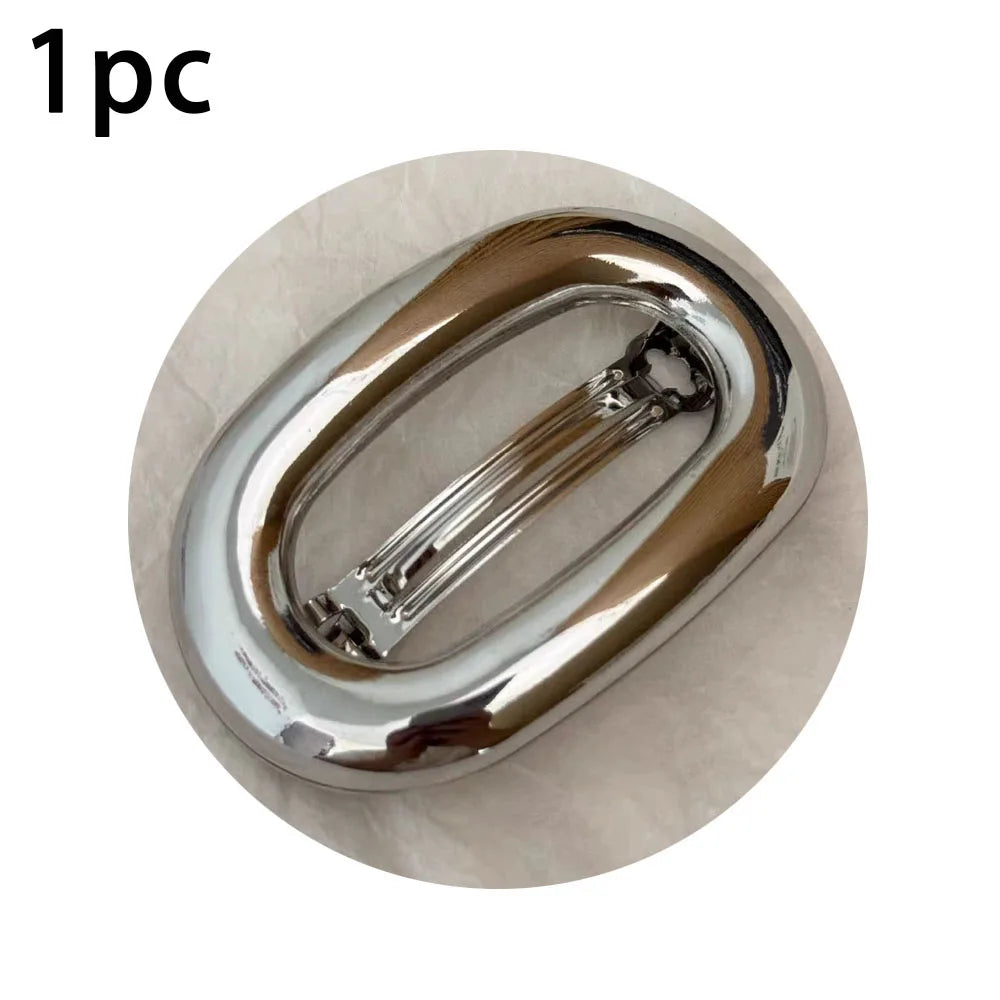 A single elegant metal oval hair clip with a smooth, polished finish.