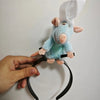 A light blue plush mouse face hair accessory with pink ears and a white cap being held by a hand.