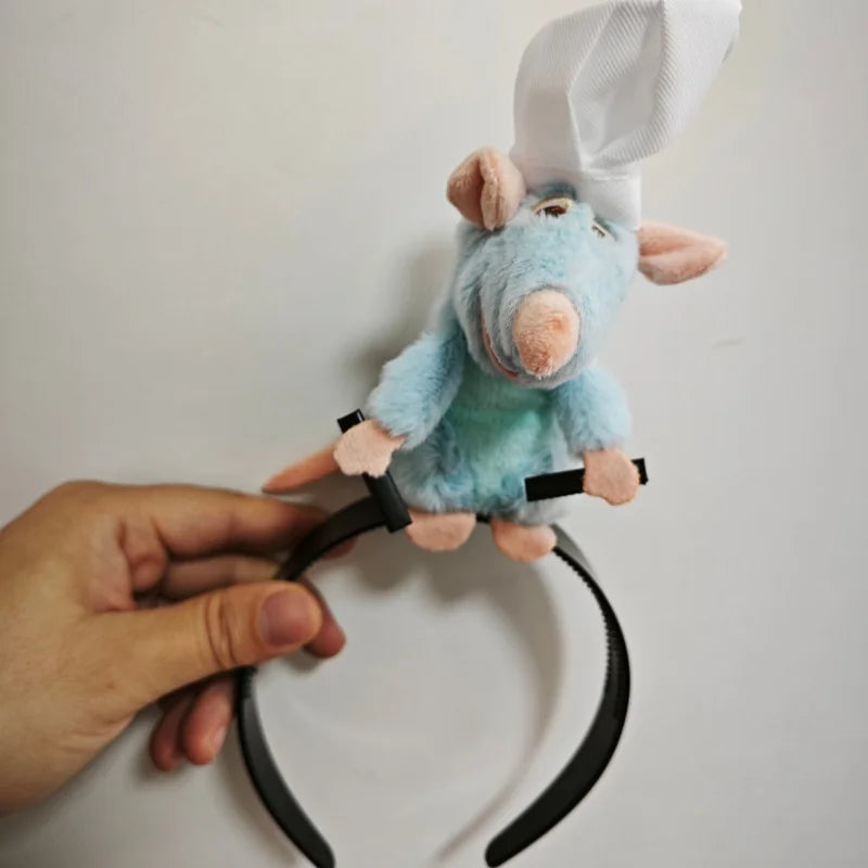 A light blue plush mouse face hair accessory with pink ears and a white cap being held by a hand.