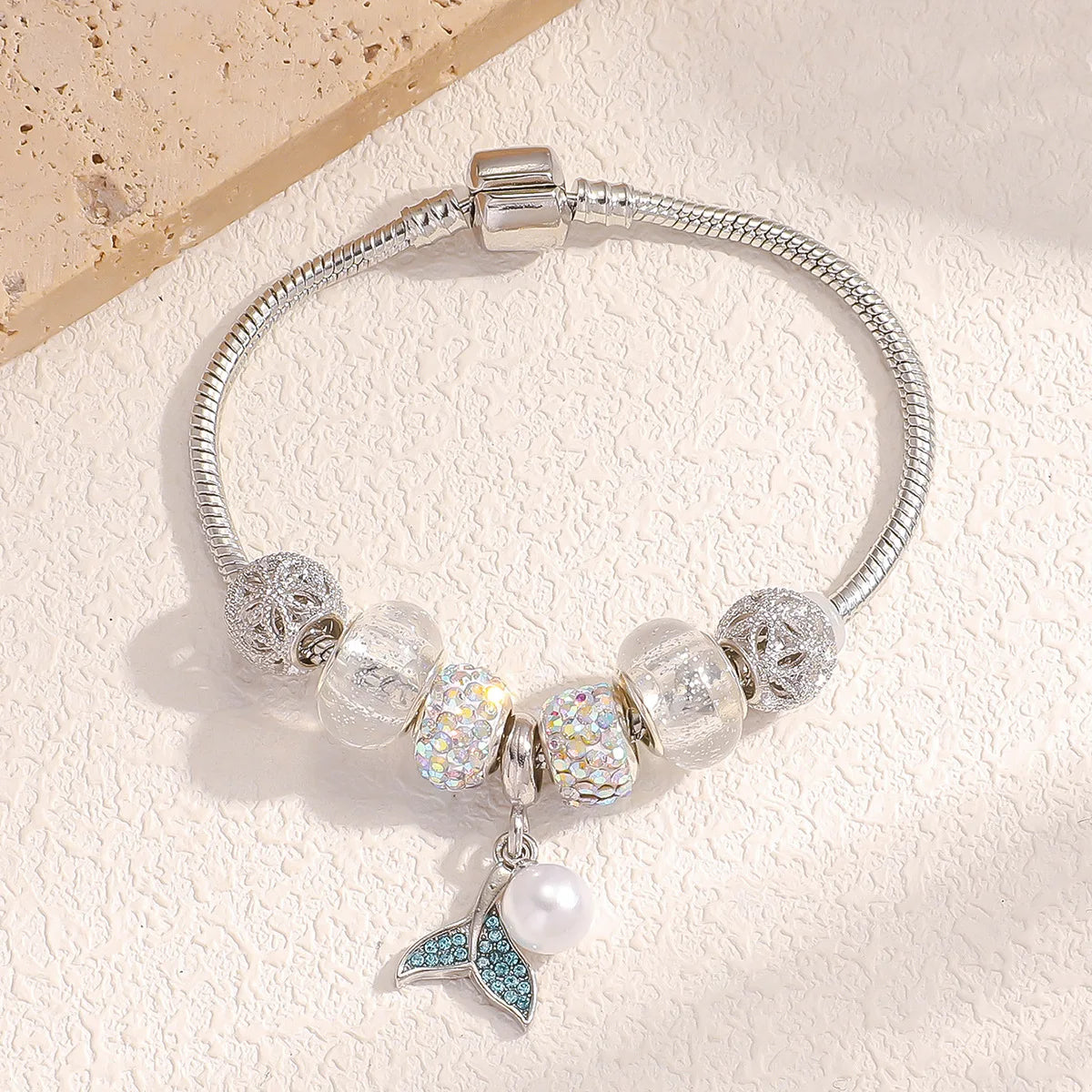 A silver bracelet featuring clear and iridescent beads, including a charm shaped like a fish tail.