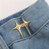 A pair of gold star-shaped decorative waist buckle buttons sewn onto a blue denim fabric.