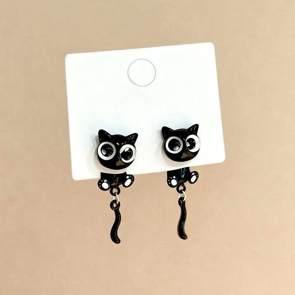 Pair of black cat stud earrings with dangling charms displayed on a white card.