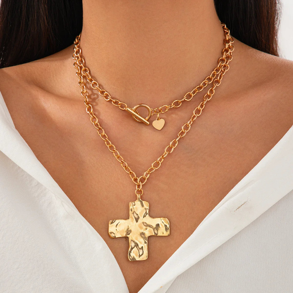 Nahaufnahme einer goldfarbenen, mehrlagigen Kreuz-Anhänger-Kette um den Hals vor hellem Hintergrund.