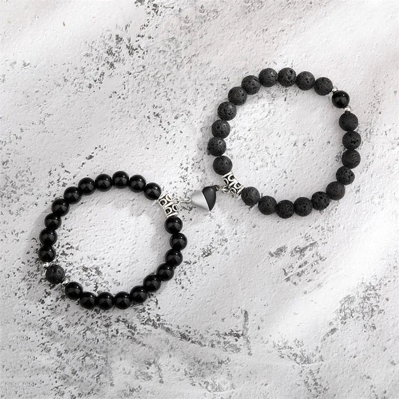 A pair of black natural stone heart couple bracelets lying on a white textured surface.