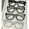 A display of five pairs of classic square reading glasses in various styles and colors.