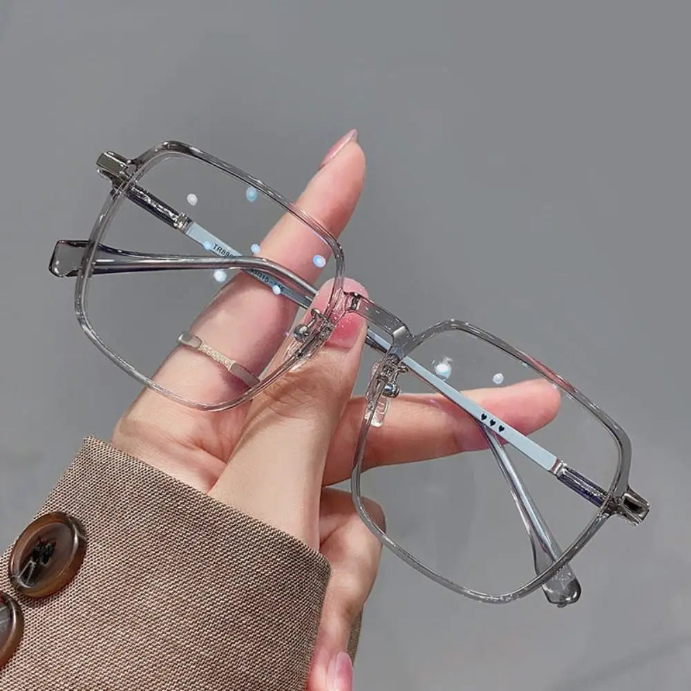 A hand holds a pair of clear metal eyeglasses with blue anti-glare coating against a gray background.