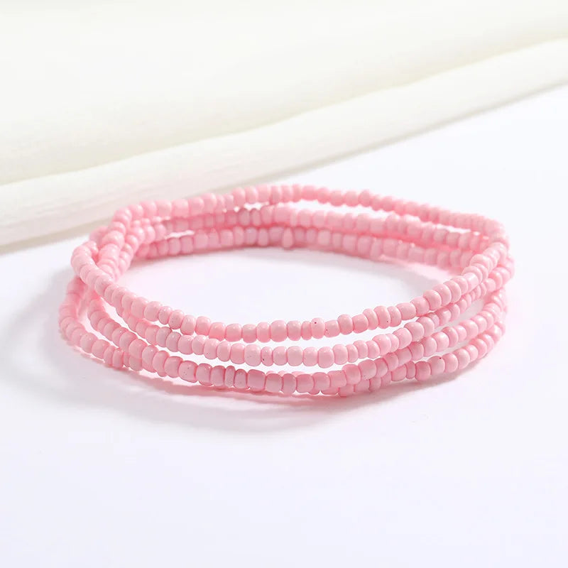 Pulsera de cadena de cuentas rosas apilada sobre una superficie blanca.