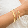 Three gold-plated stainless steel bracelets worn on a wrist against a light fabric background.