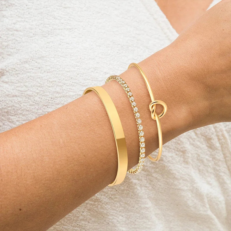 Three gold-plated stainless steel bracelets worn on a wrist against a light fabric background.