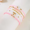 A stack of pink and white beaded bracelets with gold accents worn on a wrist.