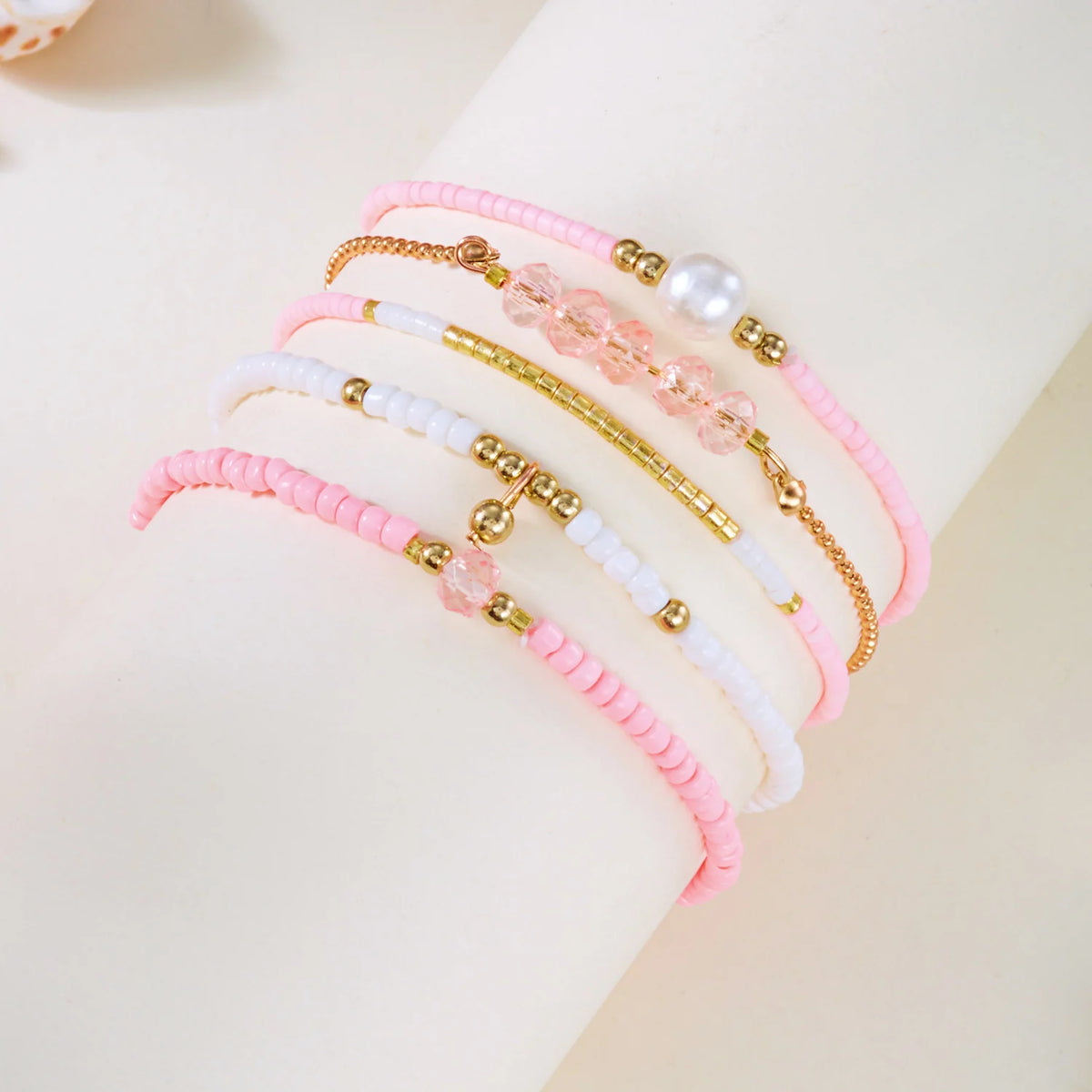A stack of pink and white beaded bracelets with gold accents worn on a wrist.