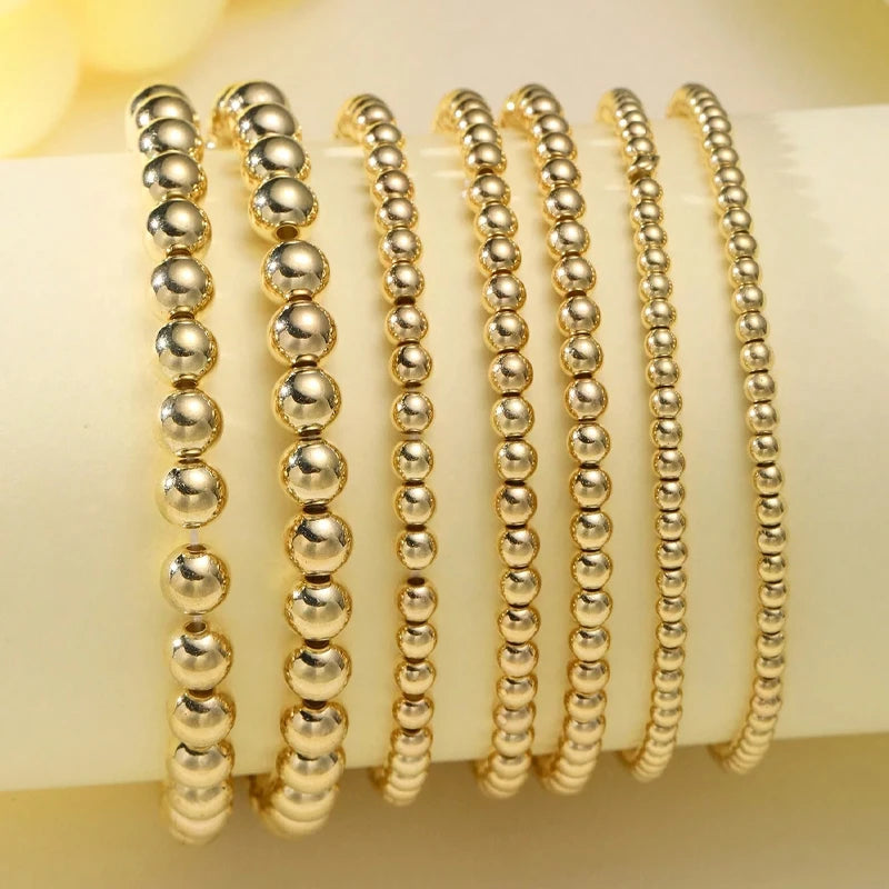 A set of minimalist round beaded bracelets in gold tone displayed on a white surface.