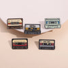 A collection of five retro cassette enamel pins featuring various labels and designs.
