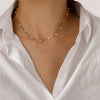 Rapproché d'une chaîne en or avec de petits charms de perles blanches portée sur un t-shirt blanc.