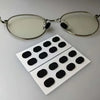 Un par de gafas transparentes con almohadillas nasales negras antideslizantes, junto a un juego de almohadillas blancas.