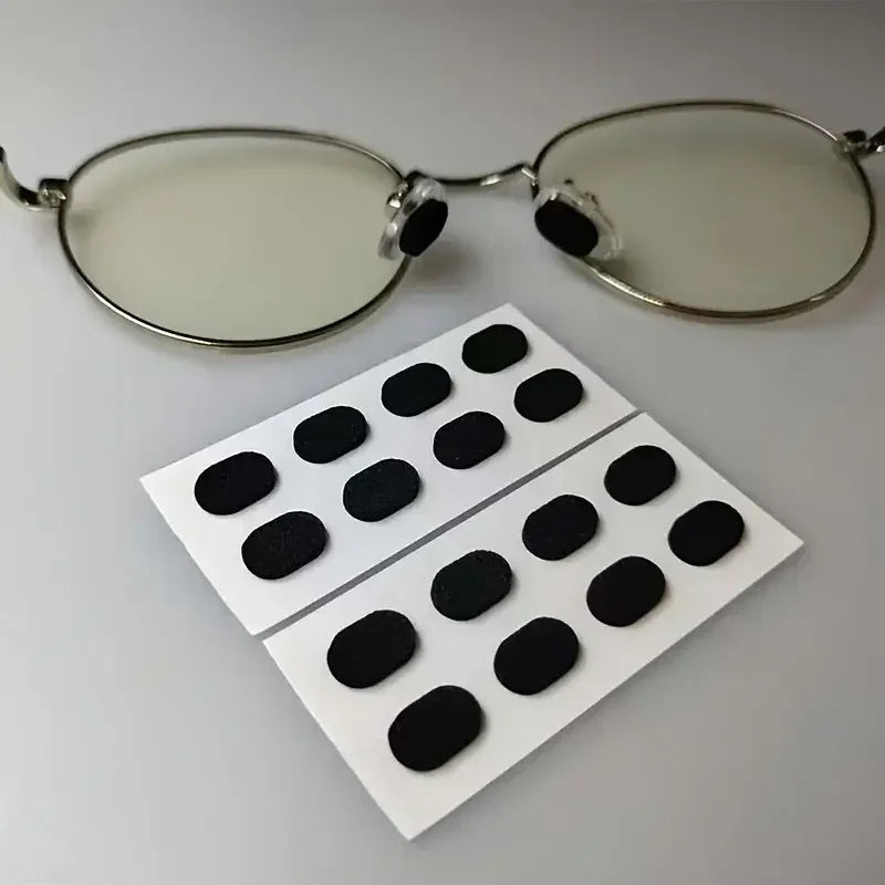 Un par de gafas transparentes con almohadillas nasales negras antideslizantes, junto a un juego de almohadillas blancas.