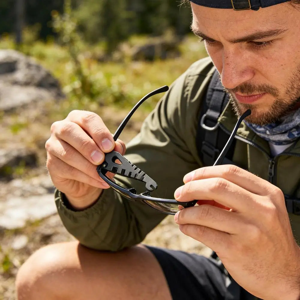 A man is using a precision eyeglass temple adjustment tool to modify eyeglasses outdoors.