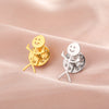 A pair of gold and silver punk stickman brooches displayed on a soft pink fabric.