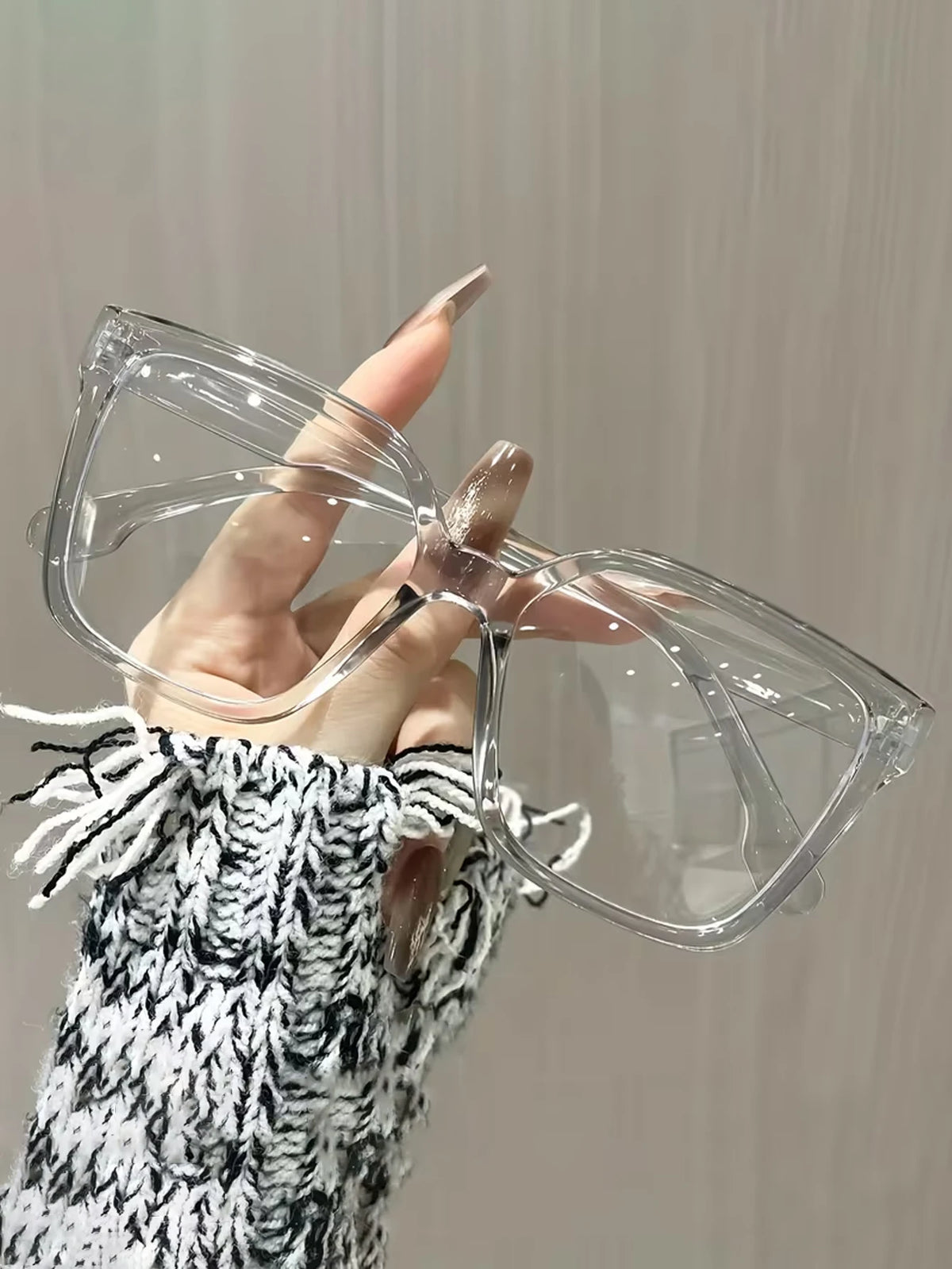 A hand wearing elegant geometric reading glasses with transparent lenses against a light background.