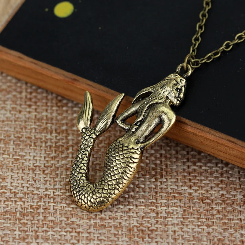 A gold-colored skull pendant necklace featuring a detailed fish or serpent design, resting on a wooden surface.
