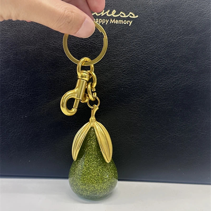 Un charm en forme de poire dorée est tenu au-dessus d'un sac velours vert foncé.