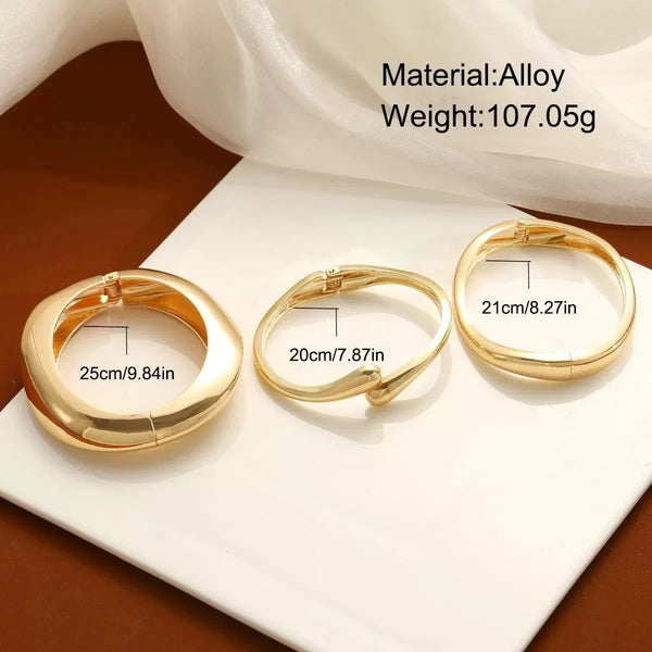 Gold alloy cuff bangle bracelet shown on a white surface with a sheer fabric background.