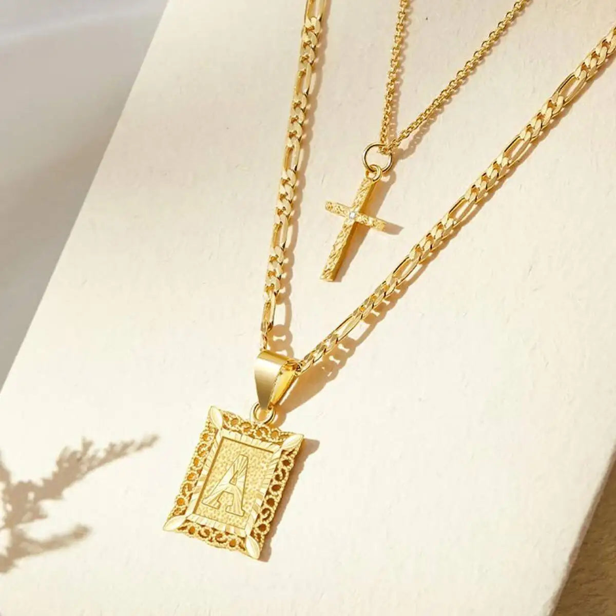 Collier pendentif lettre A en or avec un charm croix sur une chaîne délicate.