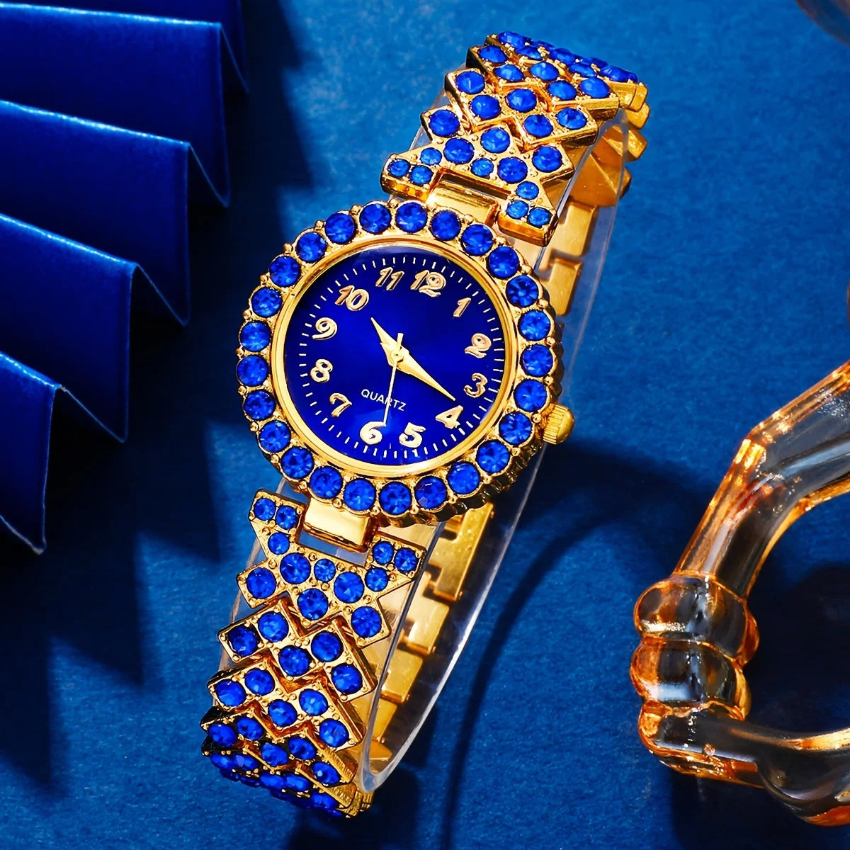 A gold-toned ladies quartz wristwatch set with a blue dial and blue stones, displayed on a blue velvet background.