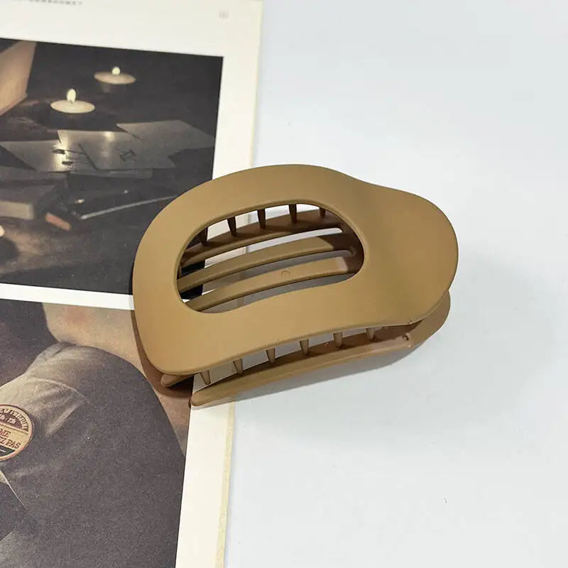 Beige ovale Haarklammer mit mehreren parallelen Zähnen neben einer Zeitschrift.