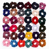A collection of six velvet scrunchies in various shades of pink, purple, red, green, and brown.
