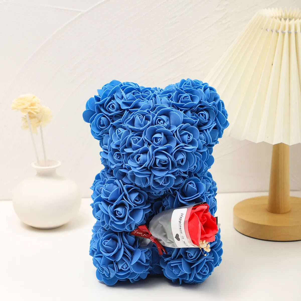 Un bouquet de roses en mousse bleues en forme de ours en peluche à côté d'un abat-jour de couleur crème.