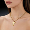 A close-up of a gold stainless steel cross pendant necklace worn around the neck against a light skin tone.