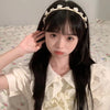 A young woman with long black hair wearing an elegant rose vine headband while sitting on a bed.
