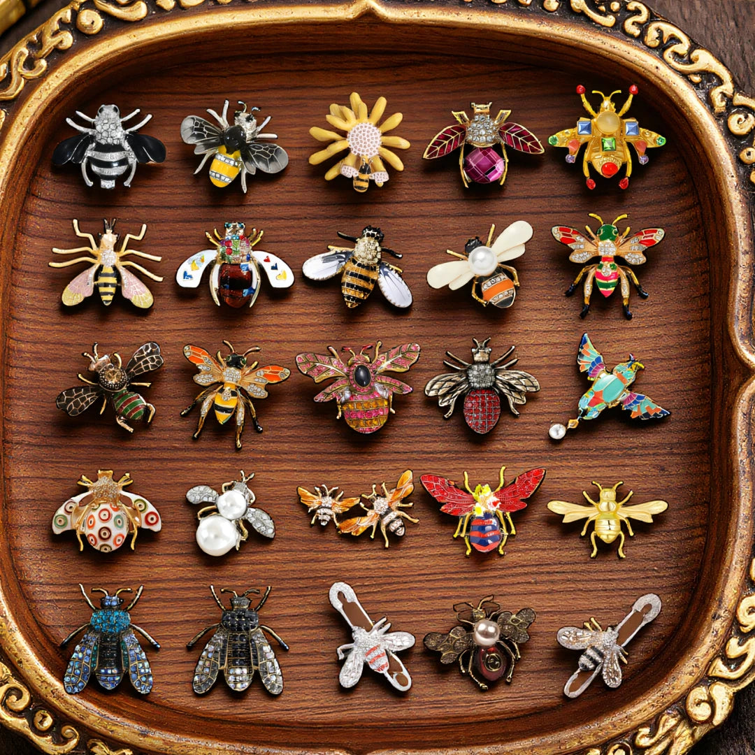 Collection de broches baroques en abeille et insectes détaillées, présentées sur un plateau en bois.