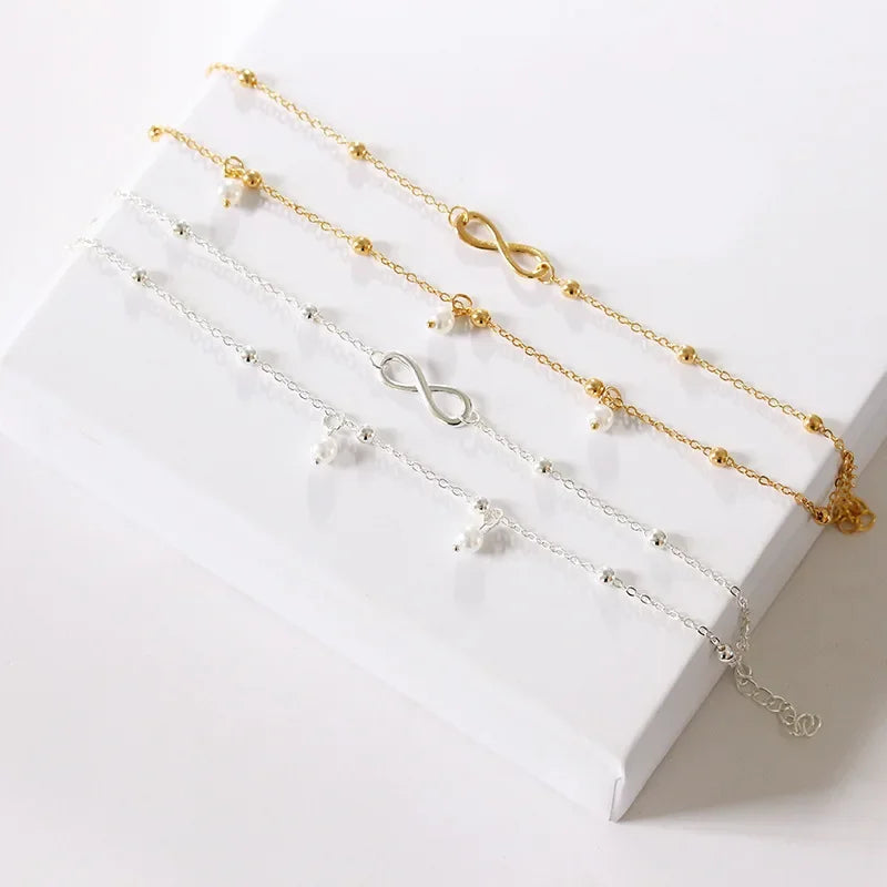 A collection of delicate silver-plated friendship anklets with various charms displayed on a white surface.