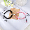 A pair of natural stone heart couple bracelets, one black and one pink, resting on a white surface with a note.