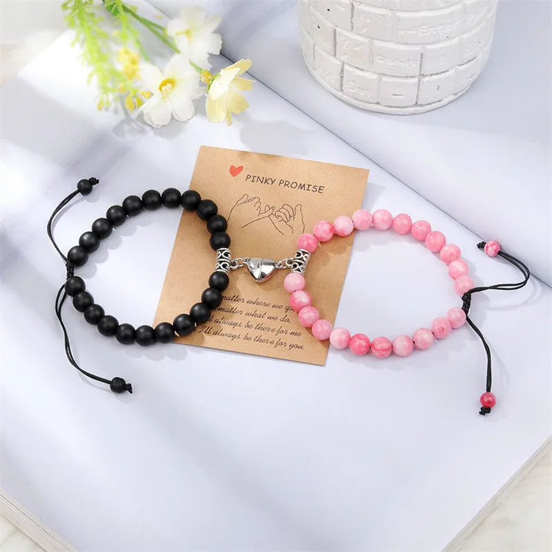 A pair of natural stone heart couple bracelets, one black and one pink, resting on a white surface with a note.