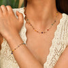 A close-up of a woman wearing a delicate necklace made of irregular colored stones against a cream knit top.