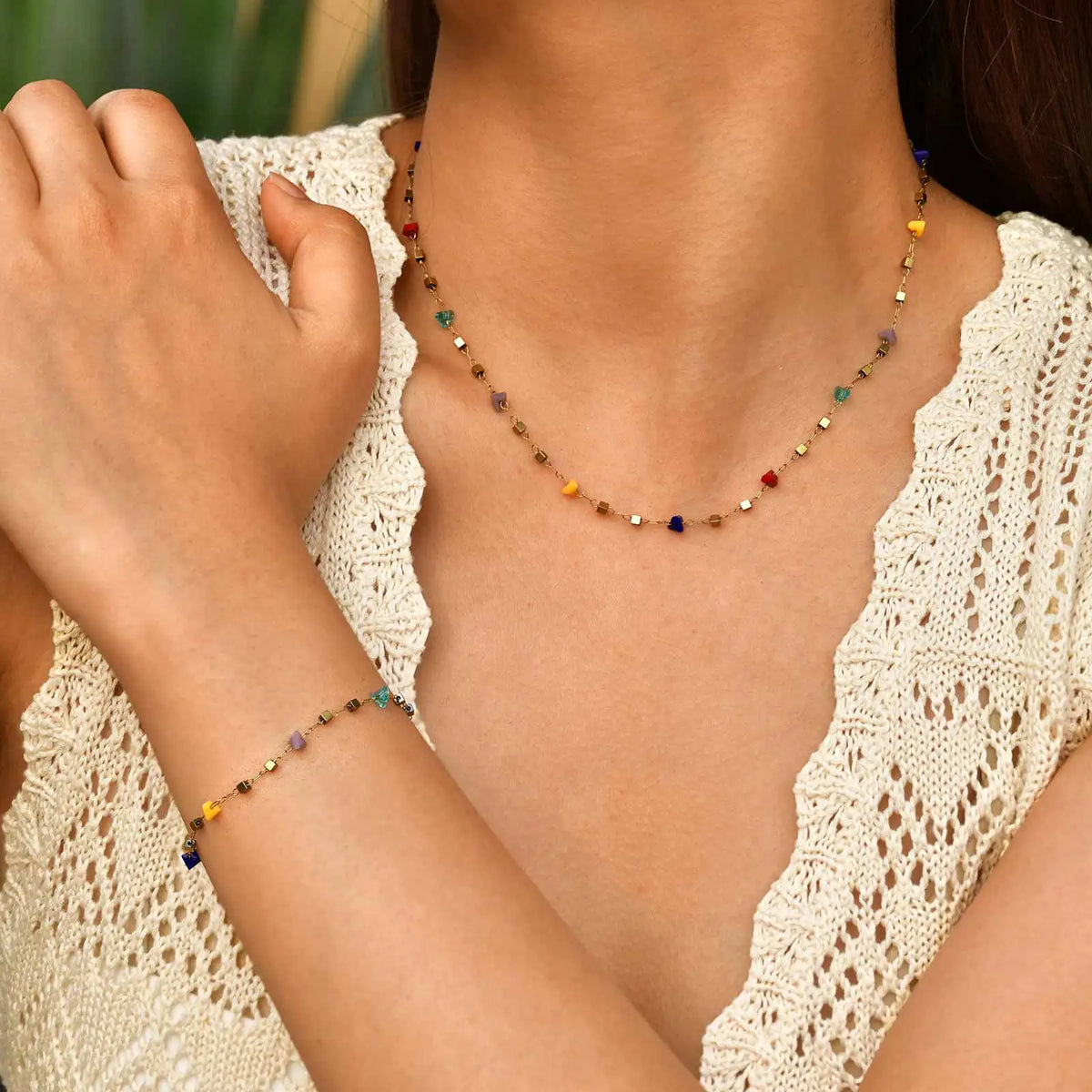 A close-up of a woman wearing a delicate necklace made of irregular colored stones against a cream knit top.
