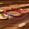 A red Turkish evil eye charm bracelet with a blue stone is displayed on a wooden surface.