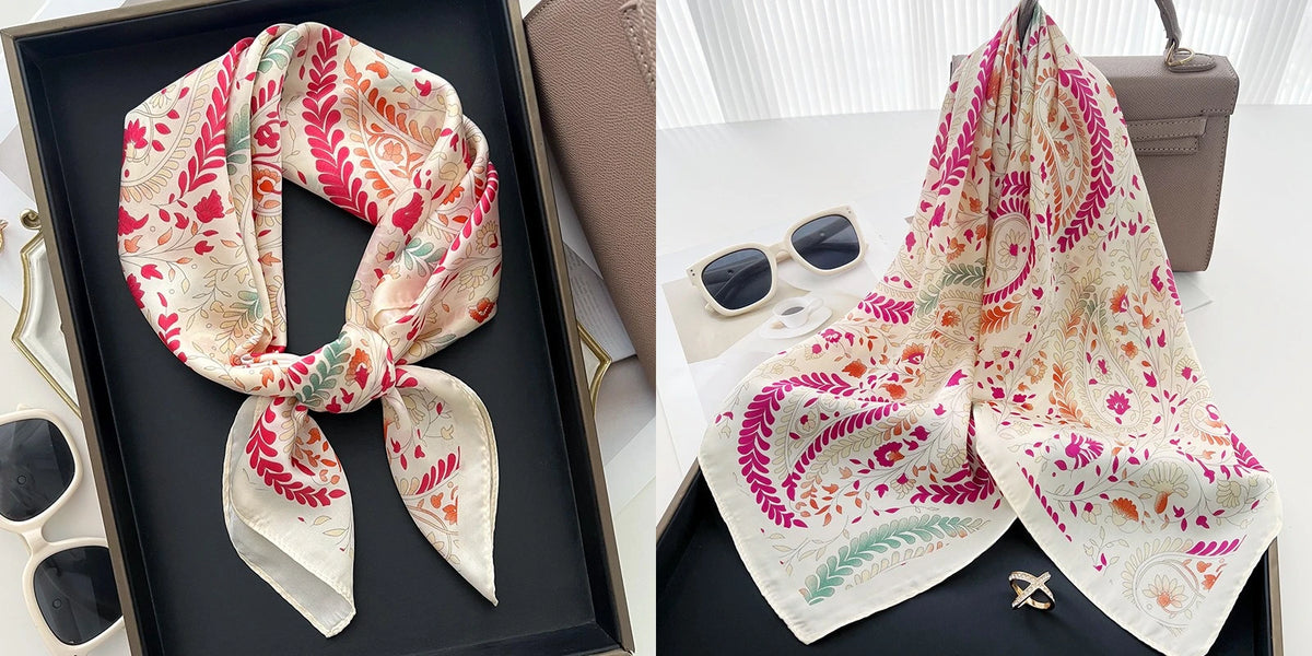 A floral print silk scarf in peach and pink tones is displayed on a dark tray.