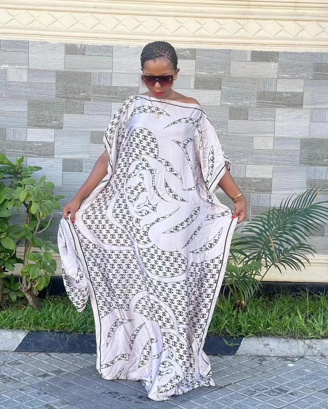 Eine Frau trägt ein fließendes, hellfarbiges Seidenkaftankleid mit schwarzem All-over-Muster im Freien.