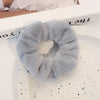 Un élastique pour cheveux en tricot flou gris clair est exposé sur une assiette blanche à côté d'une boîte.